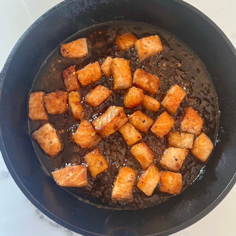 Adding the honey glaze to cooked salmon cubes