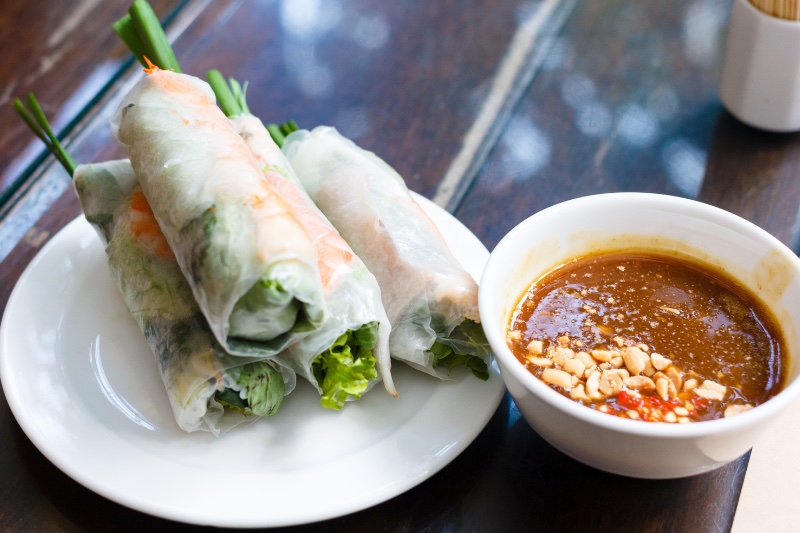 Summer rolls on a white plate next to the peanut sauce.