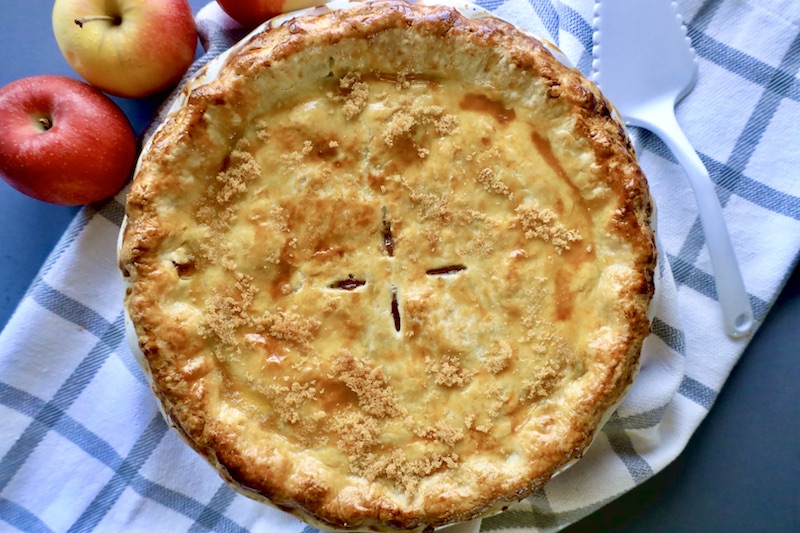 whole apple pie with fresh apples on the side and white spatula